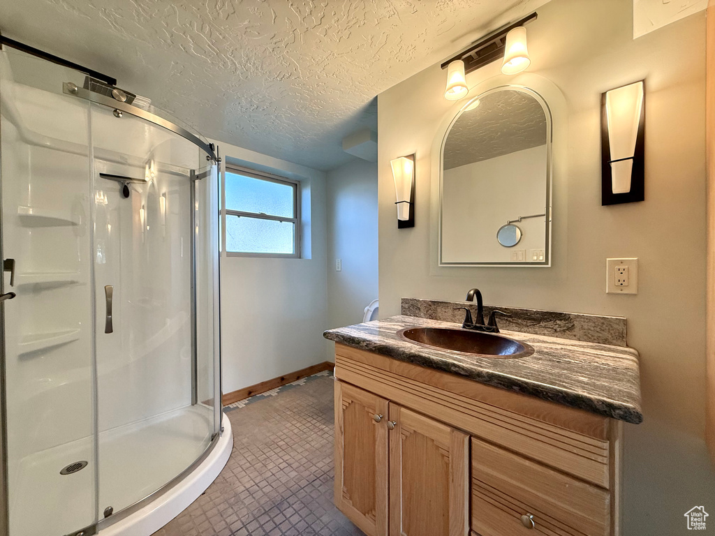 Full bathroom with a shower stall, vanity, a textured ceiling, and baseboards