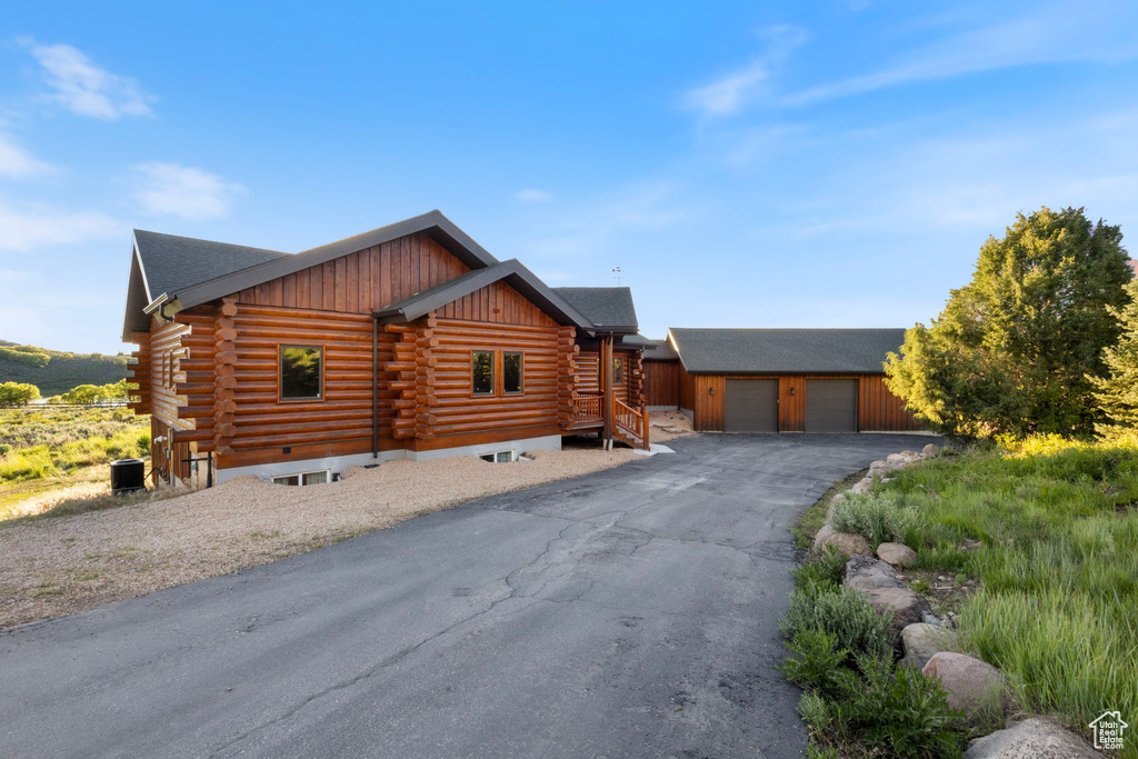 Log cabin with log exterior, an outdoor structure, a garage, and central AC unit