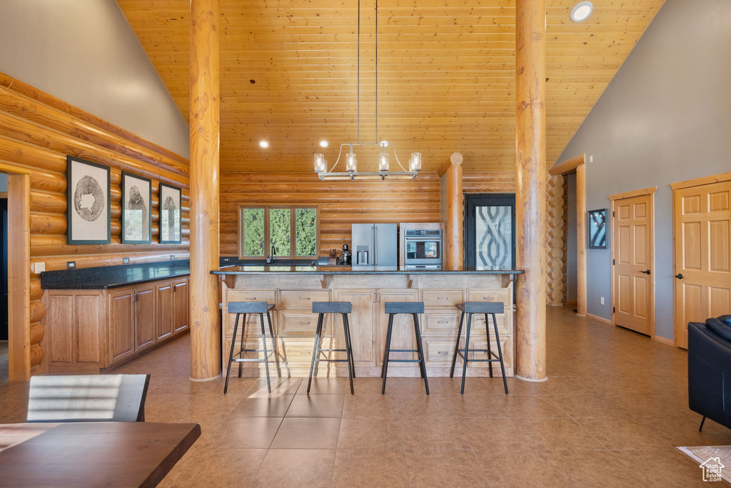 Kitchen featuring rustic walls, high vaulted ceiling, wood ceiling, stainless steel appliances, and a kitchen breakfast bar