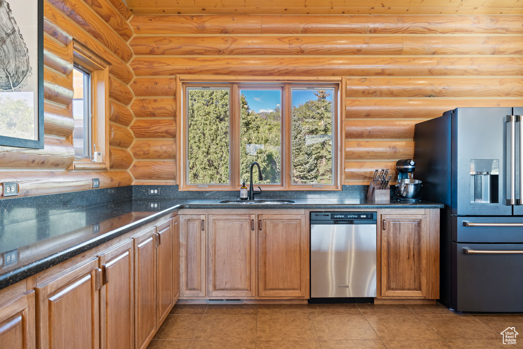 Kitchen with appliances with stainless steel finishes, log walls, a sink, light tile patterned floors, and dark stone countertops