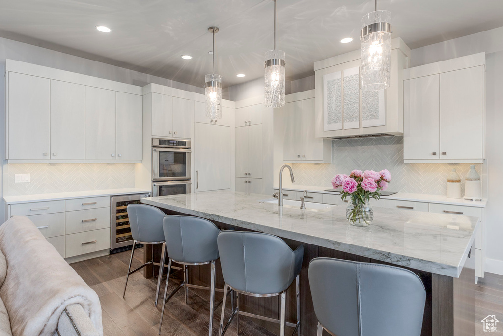 Kitchen featuring double oven, wine cooler, a sink, a breakfast bar area, and backsplash