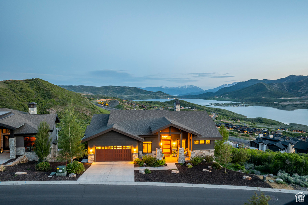 View of front of house featuring stone siding, a garage, a shingled roof, and a water and mountain view
