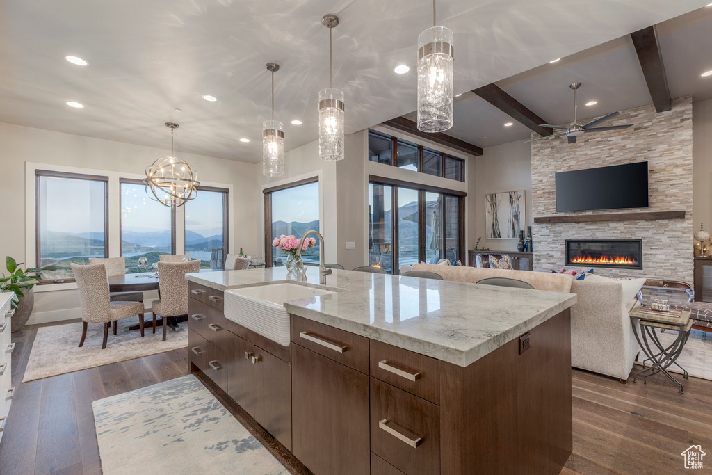 Kitchen featuring a sink, a stone fireplace, dark wood-type flooring, a ceiling fan, and beam ceiling