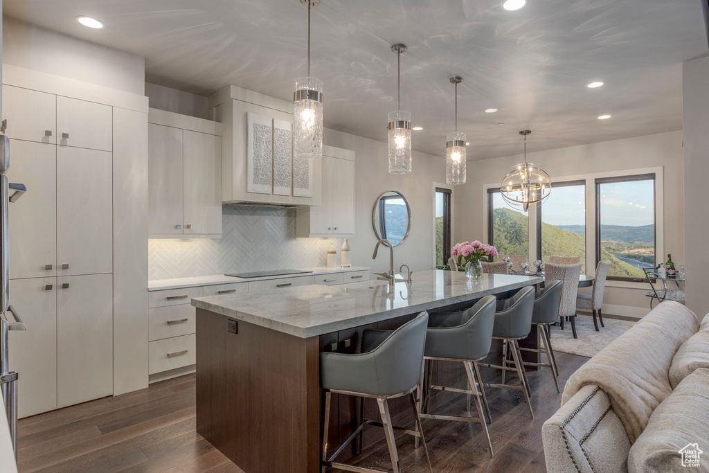 Kitchen with black electric stovetop, recessed lighting, a breakfast bar, a kitchen island with sink, and decorative backsplash