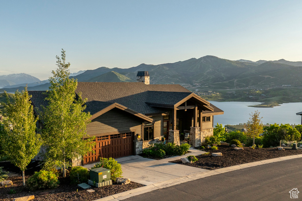 Craftsman-style home featuring a garage, driveway, a chimney, roof with shingles, and a water and mountain view