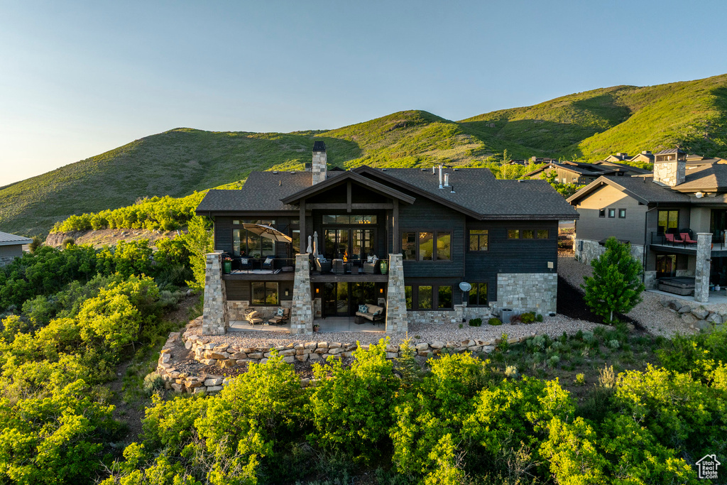 Rear view of house featuring a patio area, a balcony, stone siding, a chimney, and a mountain view
