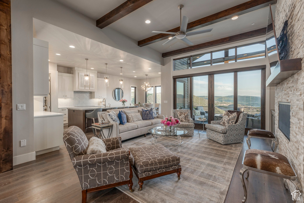 Living room with wood finished floors, ceiling fan, a chandelier, beam ceiling, and recessed lighting