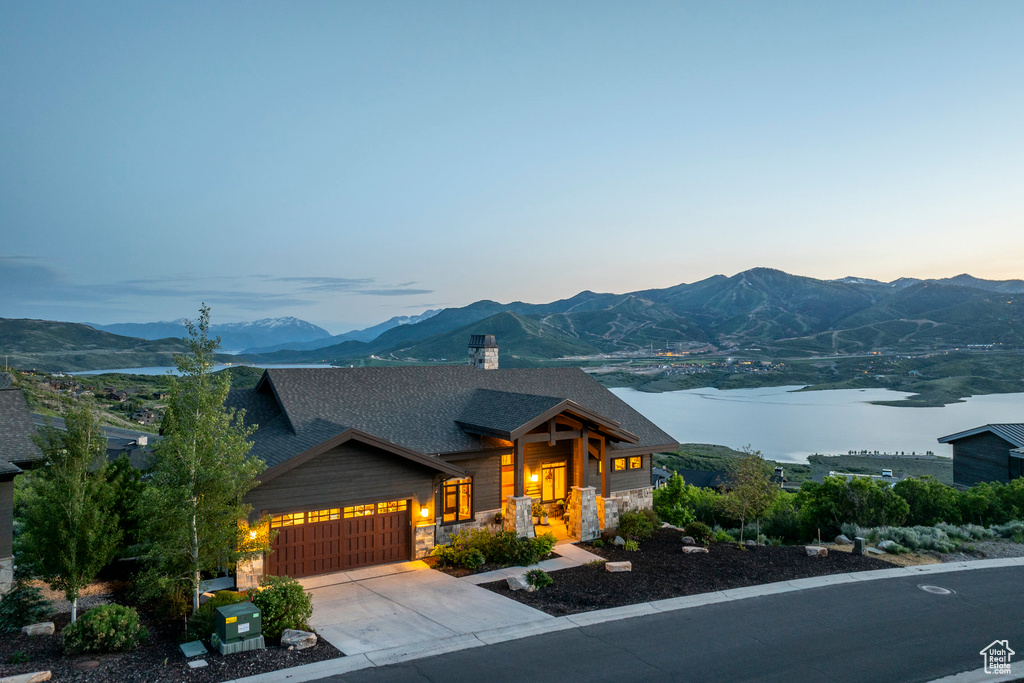 View of front of house with an attached garage, a mountain view, stone siding, roof with shingles, and driveway