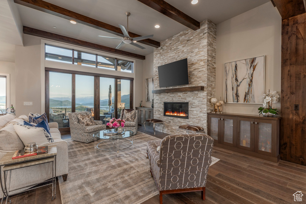 Living room with a fireplace, wood finished floors, ceiling fan, beamed ceiling, and a towering ceiling