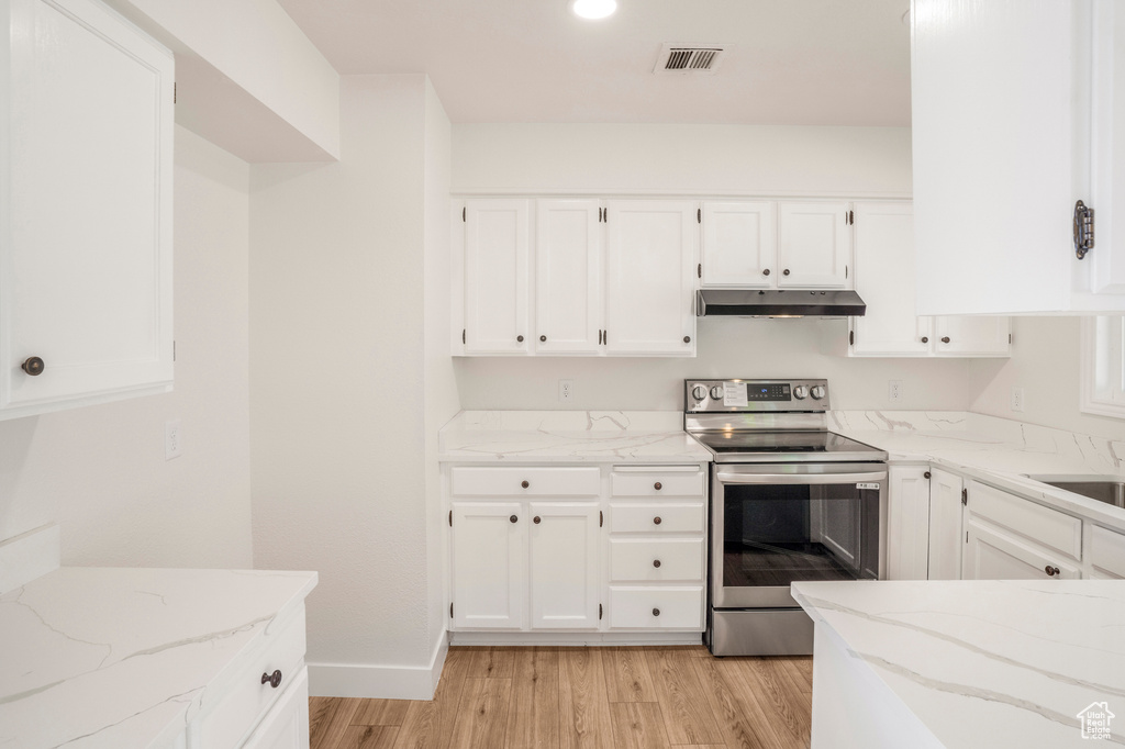 Kitchen featuring stainless steel electric range, under cabinet range hood, light wood-type flooring, light stone counters, and white cabinetry