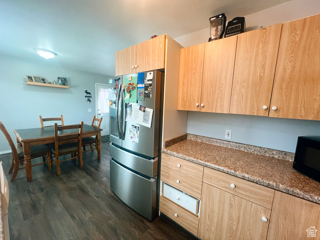 Kitchen with stainless steel refrigerator with ice dispenser, light brown cabinetry, dark wood-type flooring, and black microwave