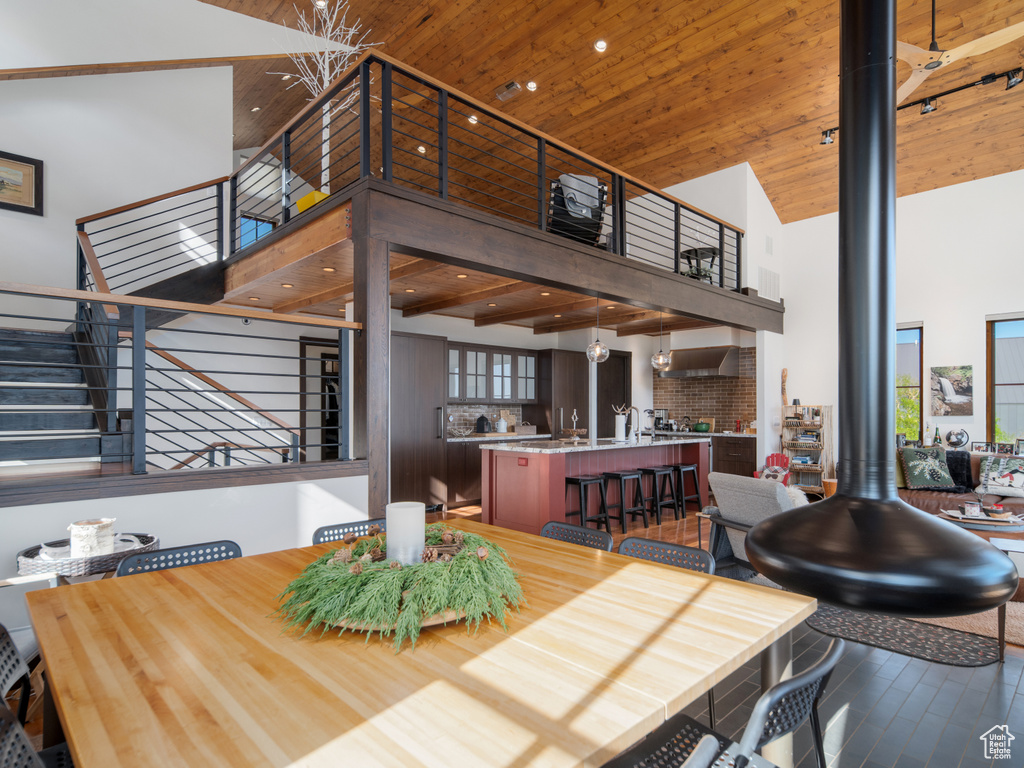 Dining area with a towering ceiling, stairway, wooden ceiling, wood finished floors, and a wood stove