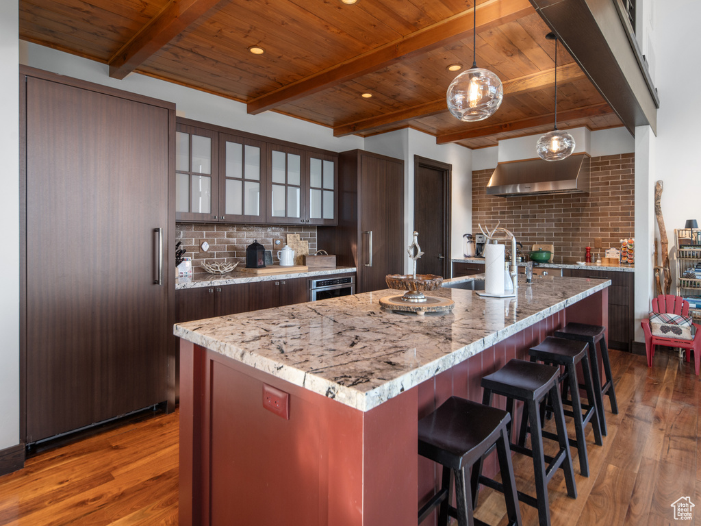 Kitchen featuring wooden ceiling with exposed beams, exhaust hood, wood finished floors, paneled built in fridge, and backsplash