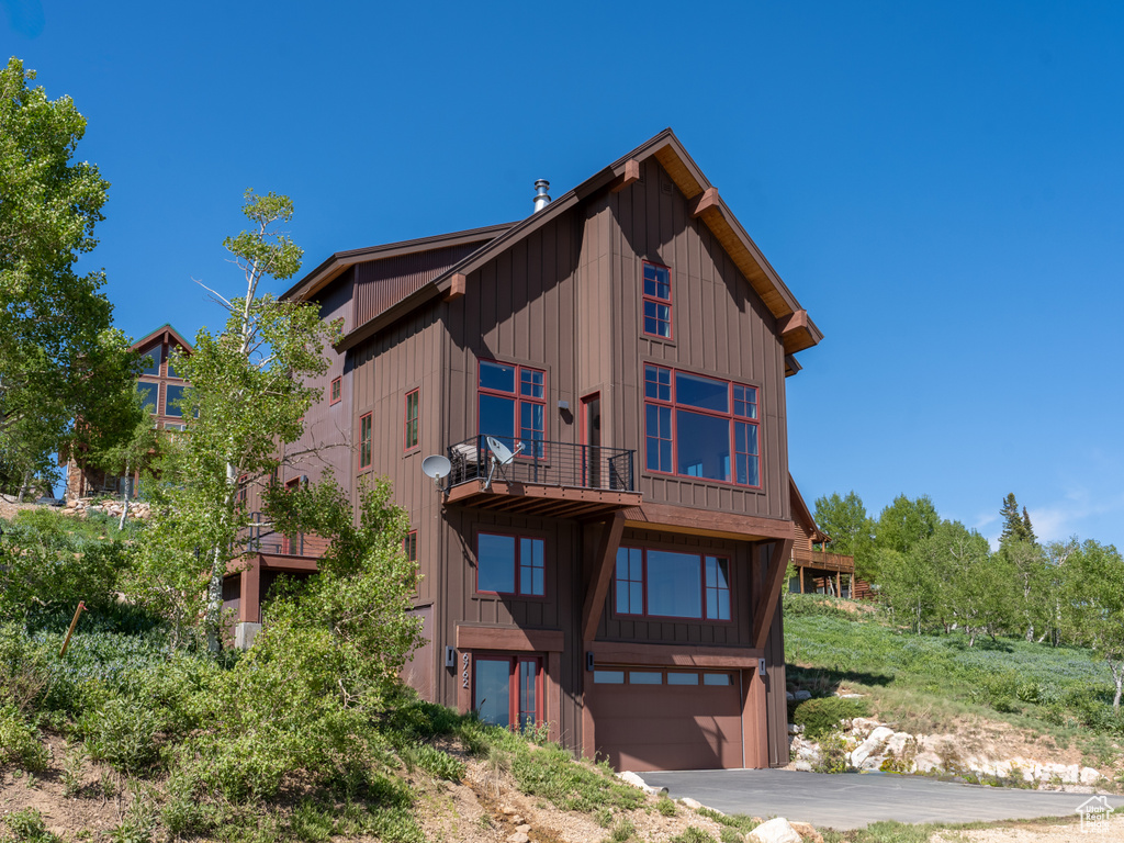 Rear view of house with a balcony, a garage, board and batten siding, and driveway