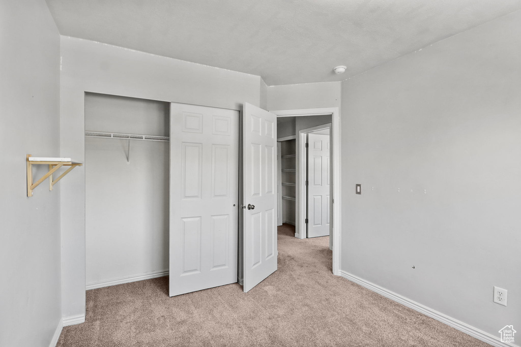 Unfurnished bedroom featuring light colored carpet, a closet, and baseboards