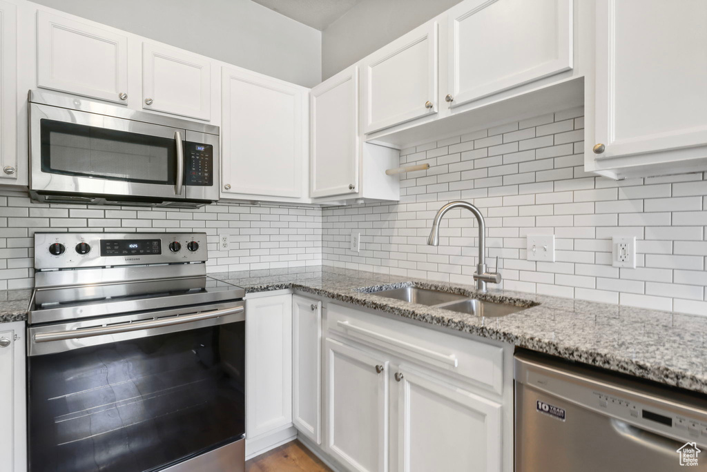 Kitchen with appliances with stainless steel finishes, a sink, white cabinets, and backsplash