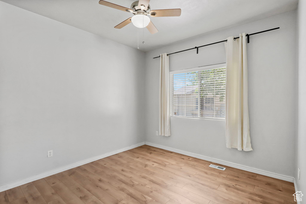 Empty room with a ceiling fan, light wood-style floors, and baseboards