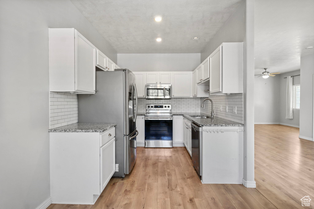 Kitchen featuring stainless steel appliances, a sink, light stone countertops, white cabinetry, and recessed lighting