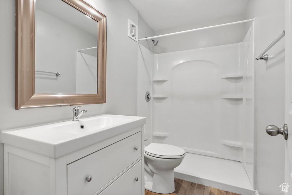 Bathroom featuring wood finished floors, vanity, toilet, and a shower