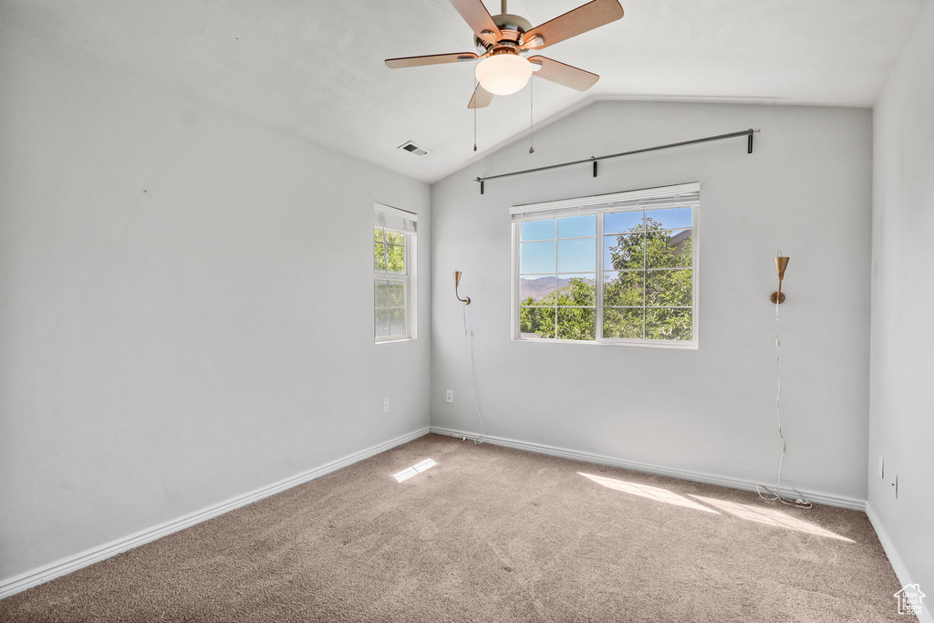 Carpeted spare room featuring lofted ceiling, ceiling fan, and baseboards