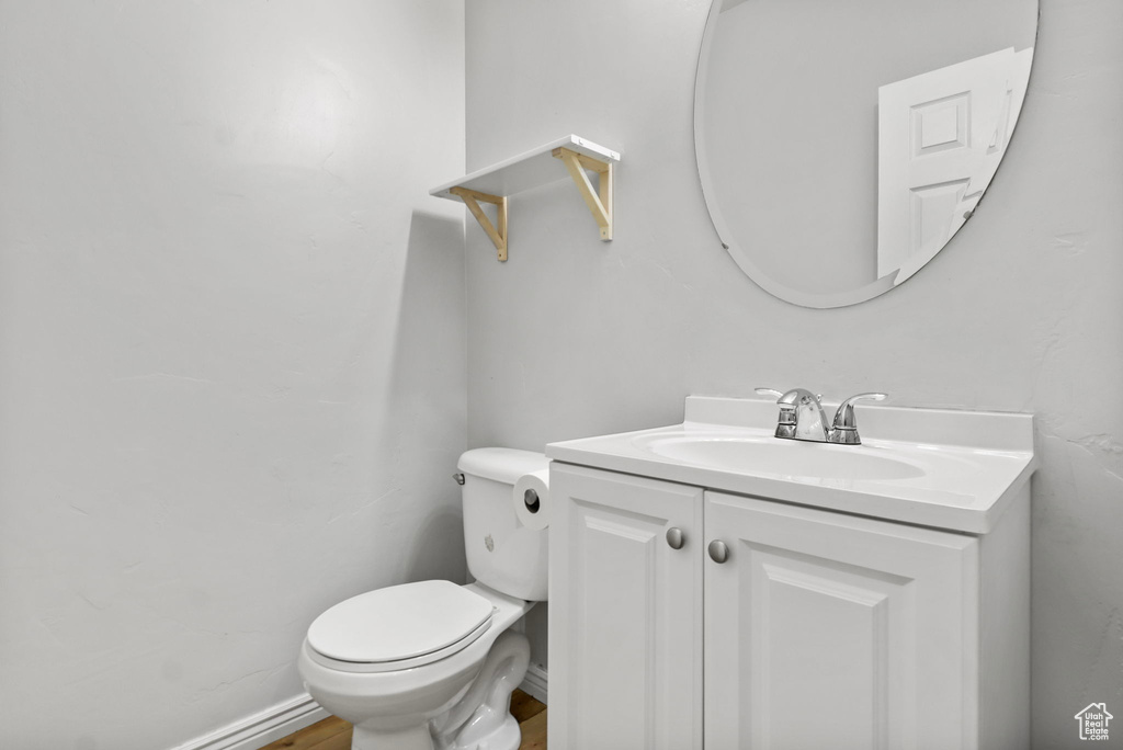 Half bathroom with vanity, toilet, and wood finished floors