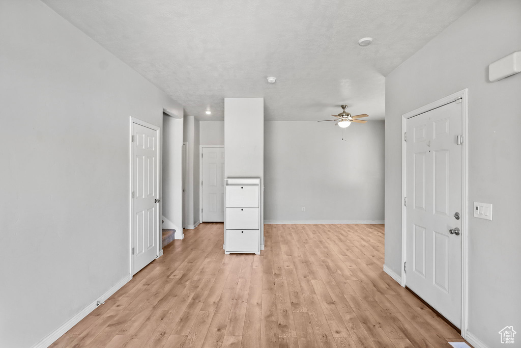 Unfurnished living room featuring a ceiling fan, light wood-type flooring, and baseboards