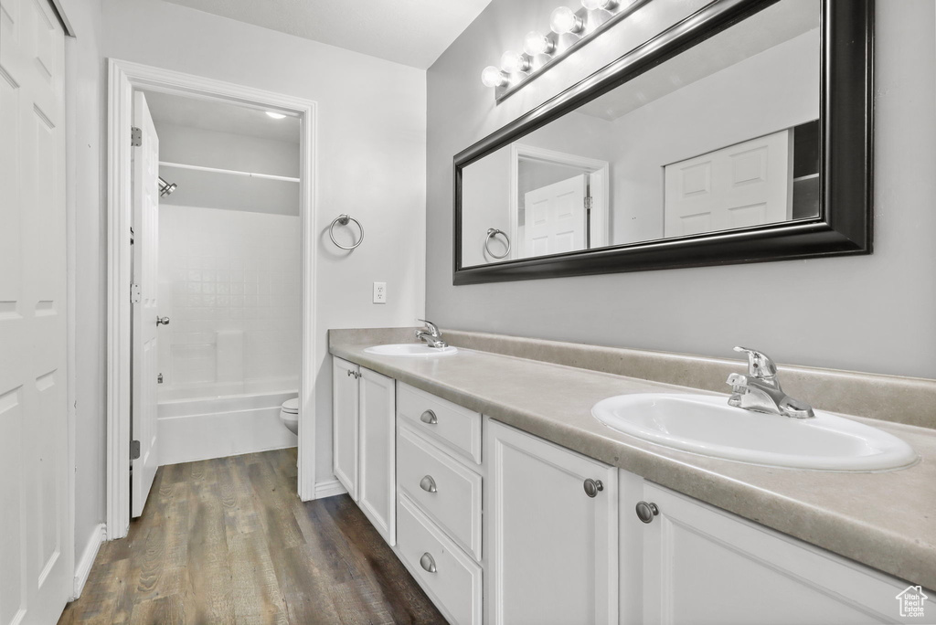 Full bath with double vanity, wood finished floors, toilet, and washtub / shower combination