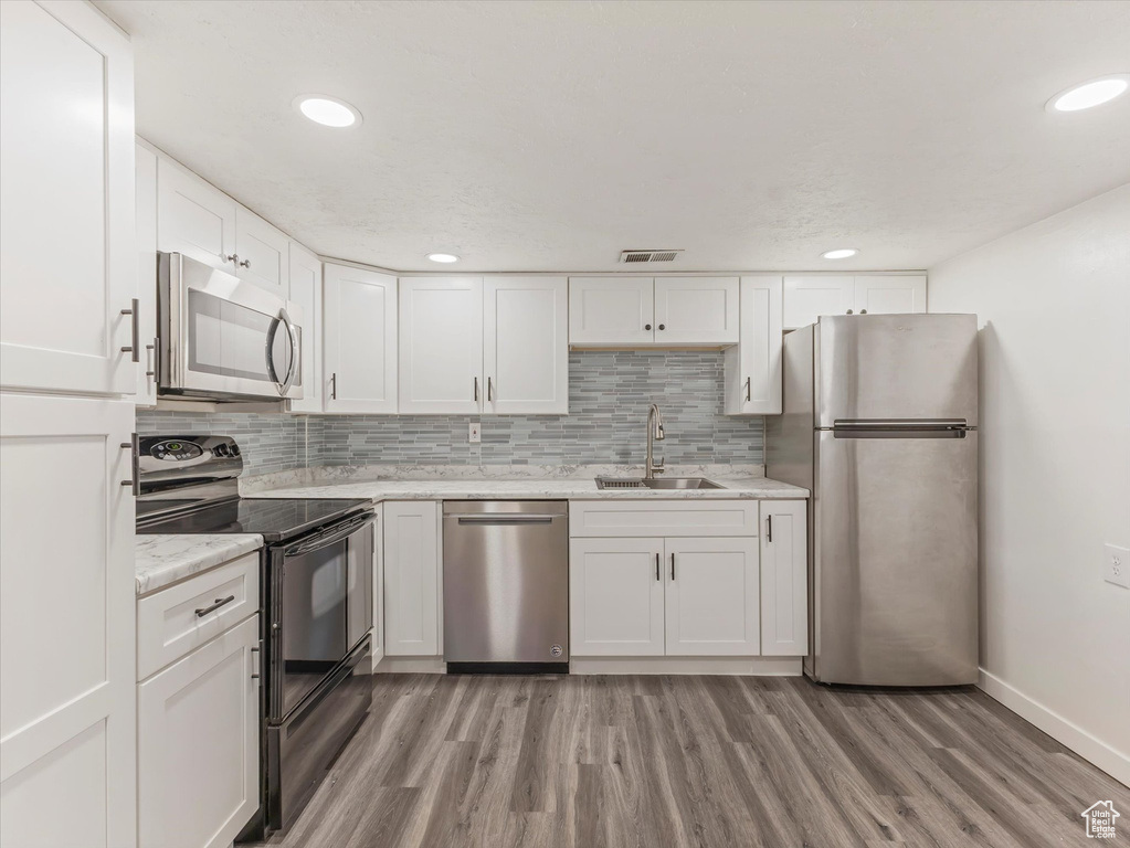 Kitchen with stainless steel appliances, a sink, white cabinets, light wood-style floors, and baseboards