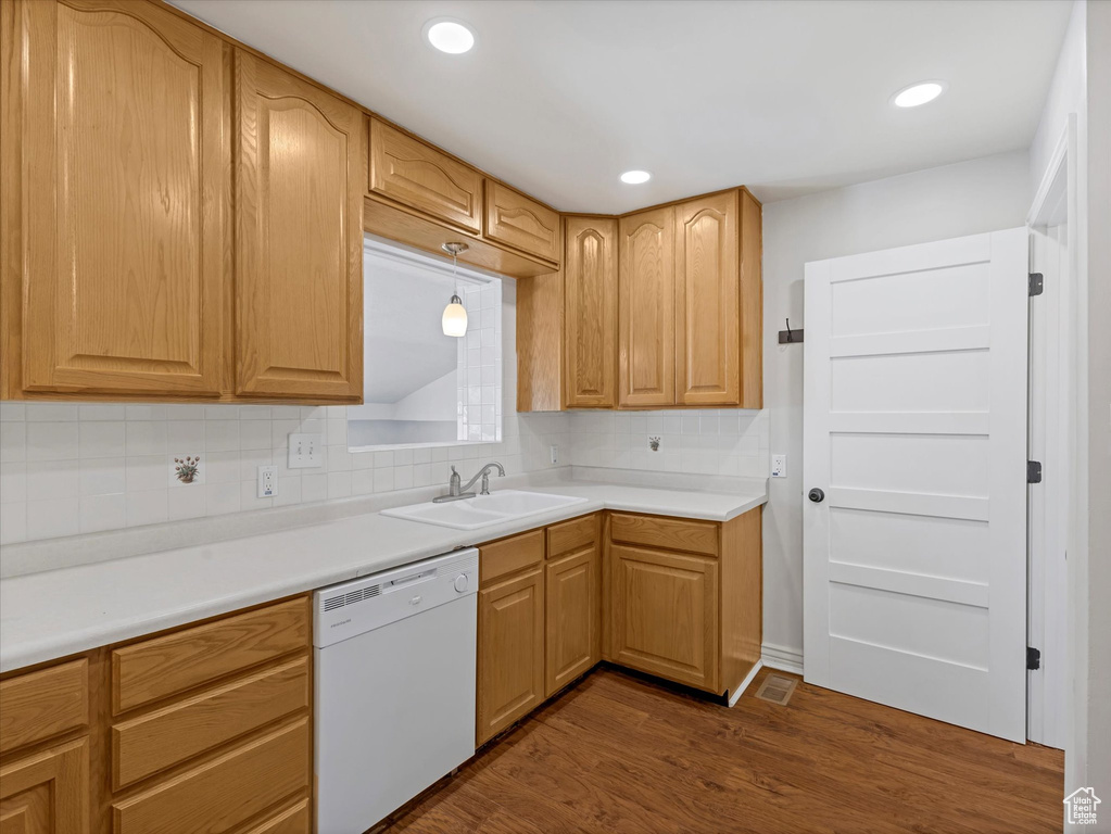 Kitchen with white dishwasher, a sink, dark wood-style floors, backsplash, and light countertops