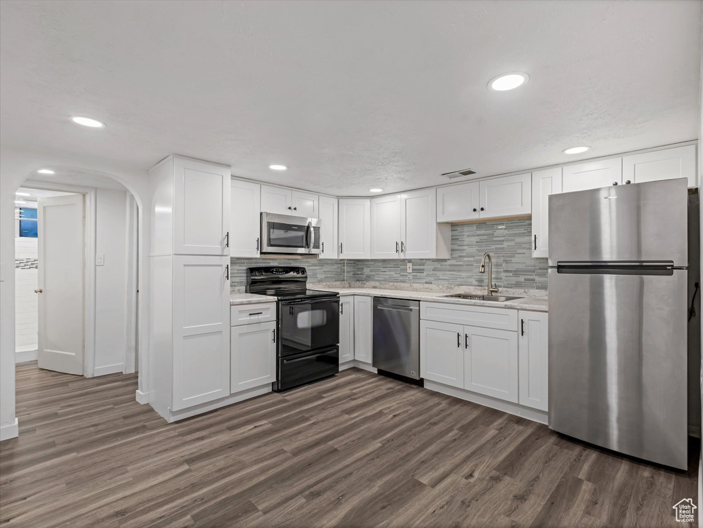 Kitchen featuring stainless steel appliances, a sink, dark wood finished floors, white cabinets, and arched walkways
