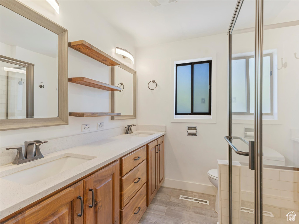 Bathroom featuring toilet, double vanity, a stall shower, baseboards, and wood finished floors