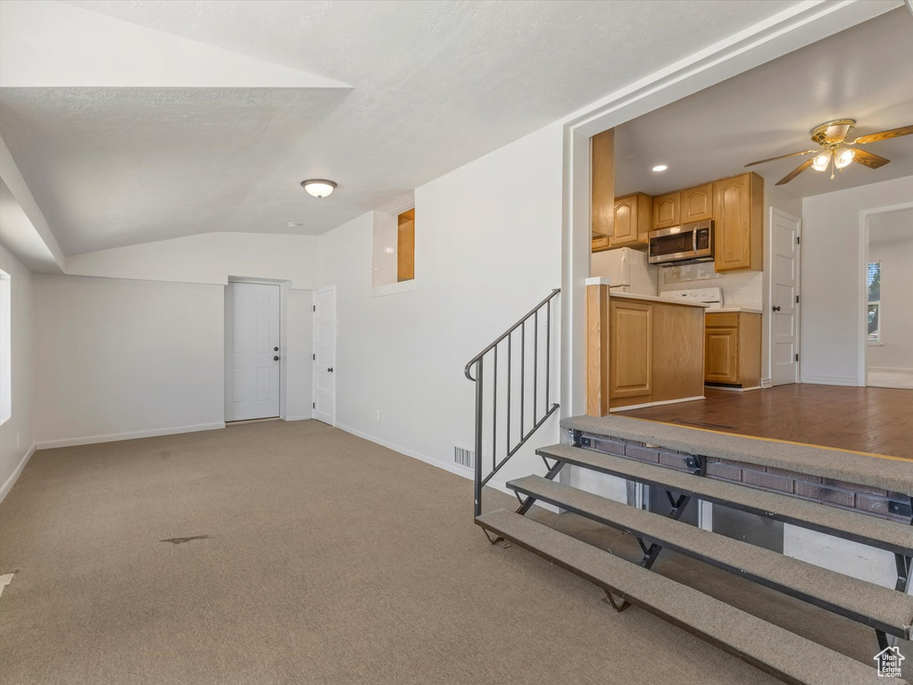Unfurnished living room with vaulted ceiling, baseboards, ceiling fan, stairs, and carpet