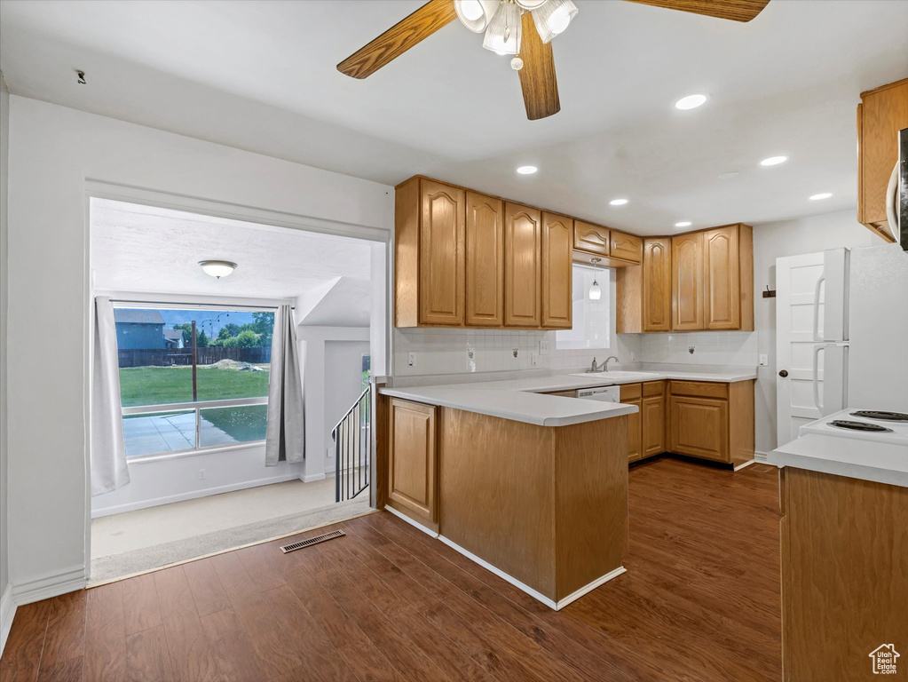 Kitchen with dark wood-type flooring, a ceiling fan, a peninsula, a sink, and light countertops