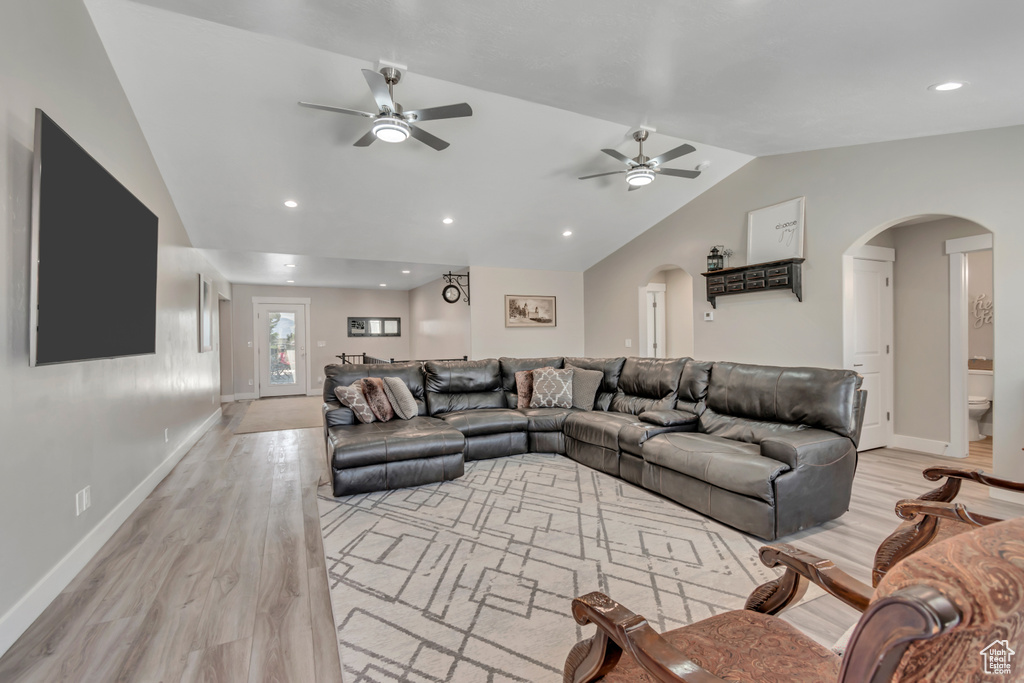 Living room featuring lofted ceiling, ceiling fan, arched walkways, light wood-style flooring, and baseboards