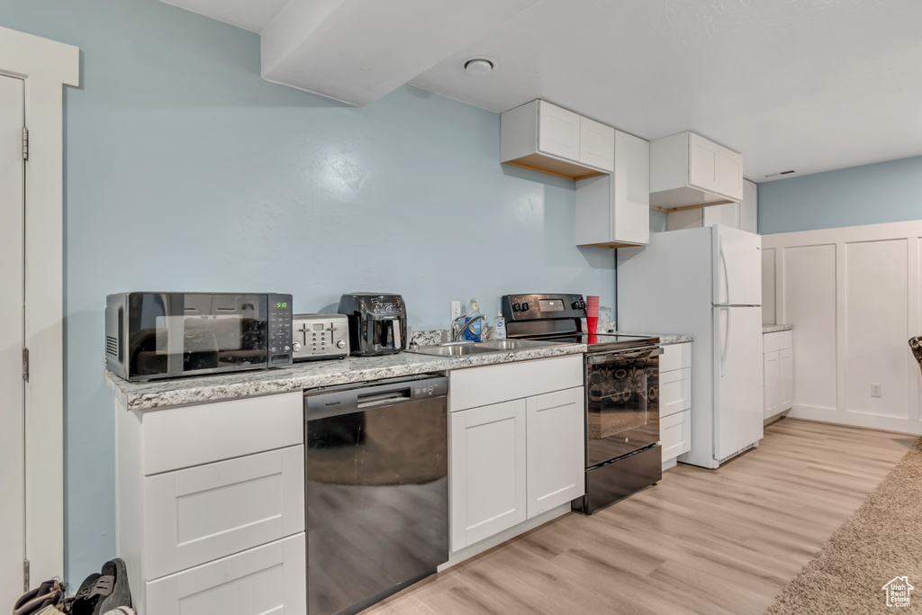 Kitchen featuring dishwashing machine, black range with electric cooktop, freestanding refrigerator, and light wood finished floors