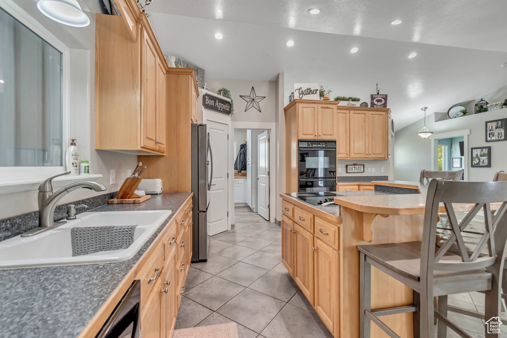 Kitchen with a sink, black appliances, a kitchen bar, light brown cabinetry, and a kitchen island