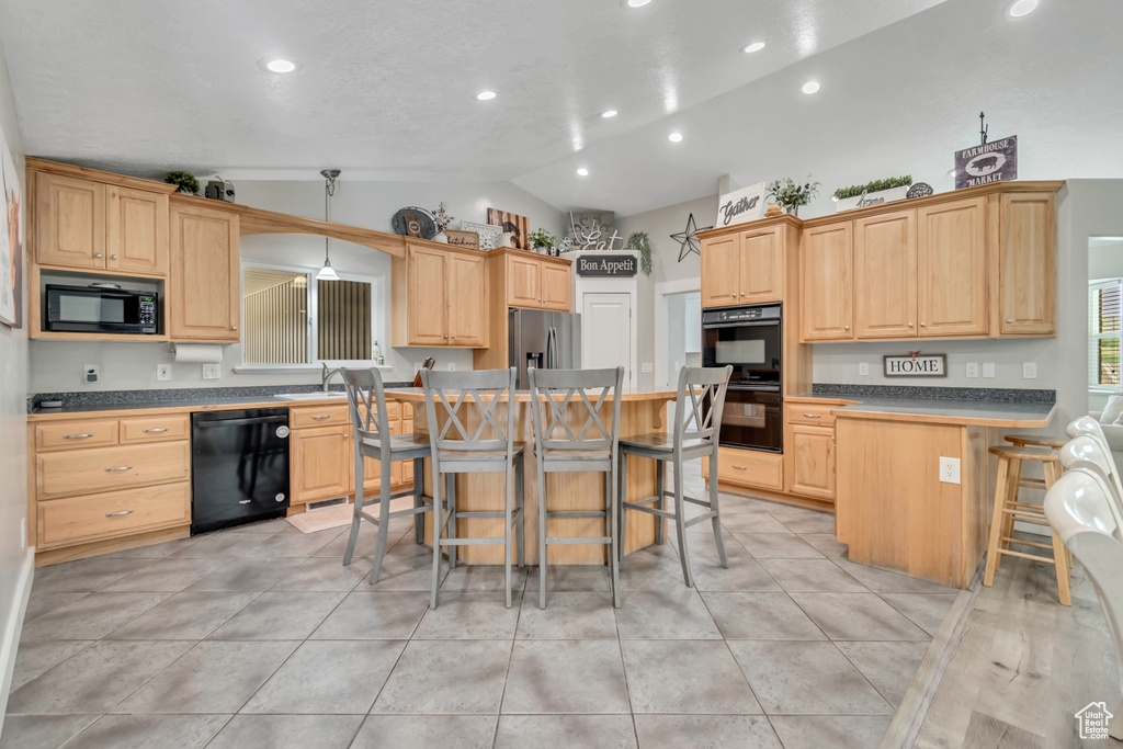 Kitchen featuring black appliances, vaulted ceiling, a kitchen bar, light brown cabinets, and light tile patterned floors