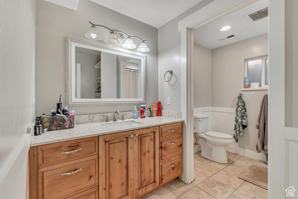 Bathroom featuring vanity, toilet, a wainscoted wall, and tile patterned flooring