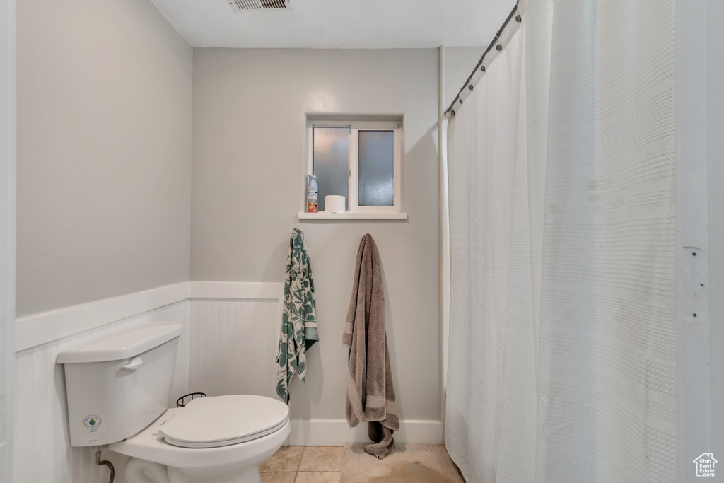 Full bath featuring wainscoting, toilet, tile patterned floors, and curtained shower