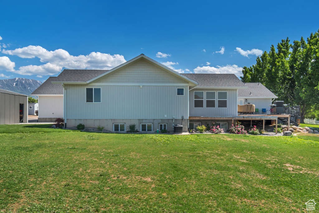 Rear view of property featuring a wooden deck, central AC, and a yard