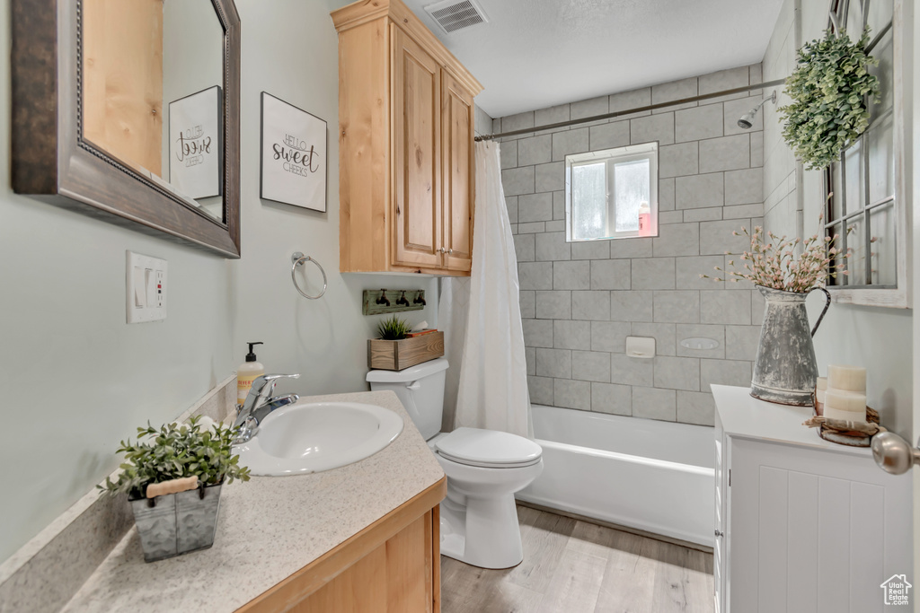 Full bath with toilet, wood finished floors, shower / bath combination with curtain, and vanity