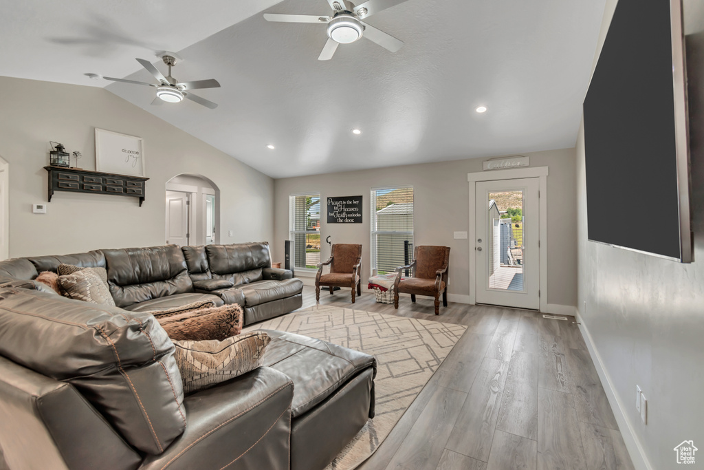Living area featuring ceiling fan, lofted ceiling, light wood-style flooring, arched walkways, and baseboards