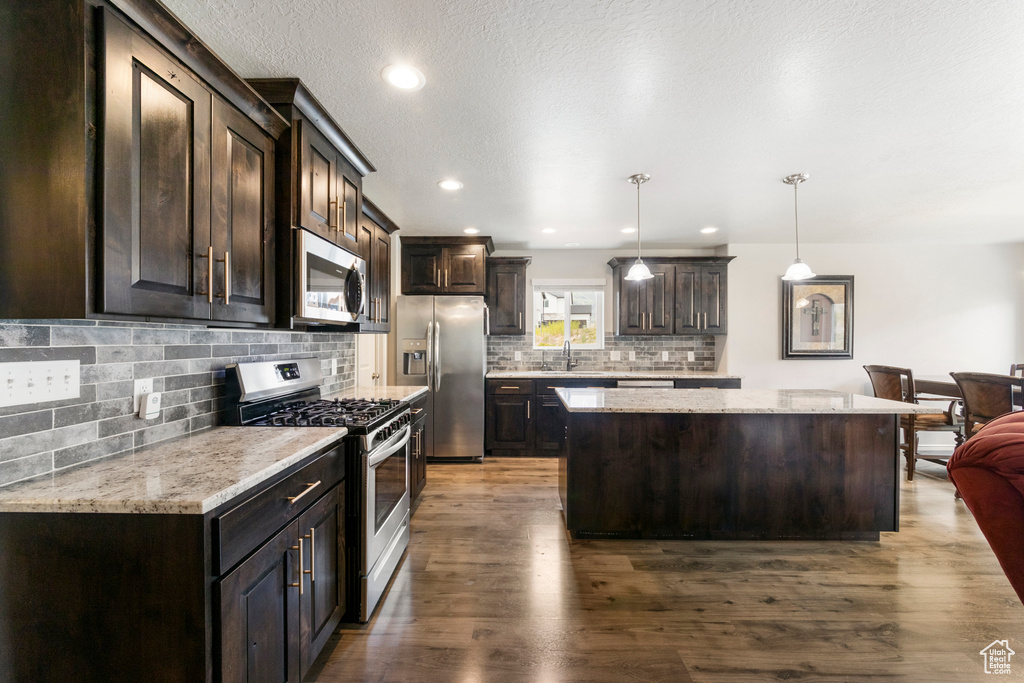 Kitchen featuring appliances with stainless steel finishes, a center island, dark brown cabinetry, tasteful backsplash, and dark wood-style flooring