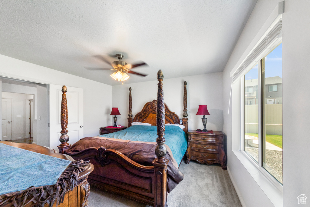 Bedroom featuring multiple windows, light colored carpet, ceiling fan, baseboards, and a textured ceiling
