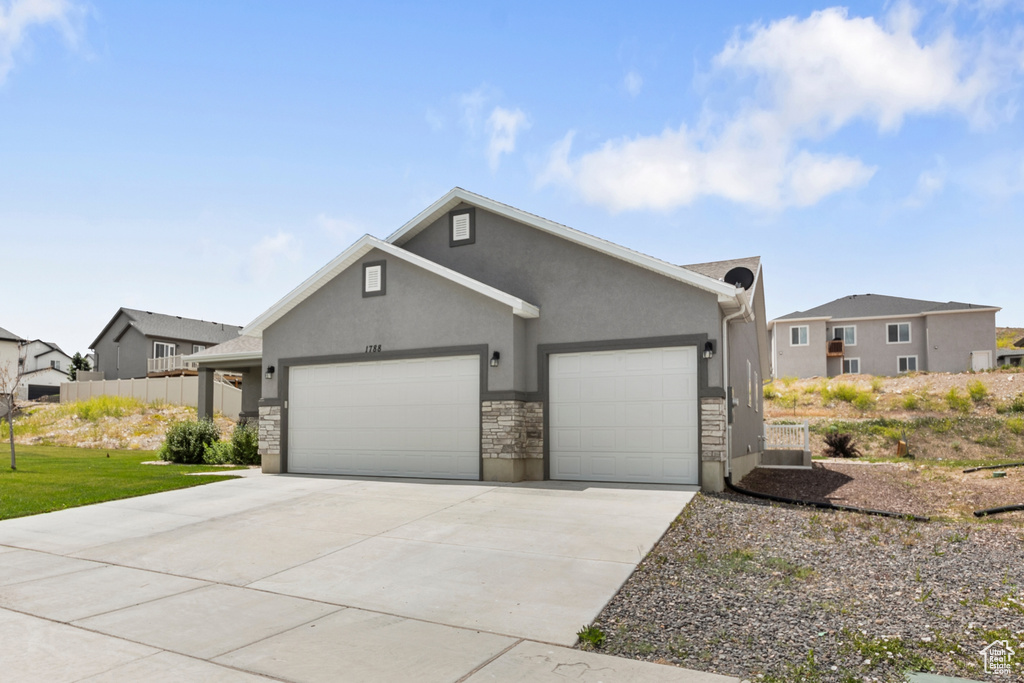 View of front facade featuring a garage, stucco siding, driveway, and stone siding