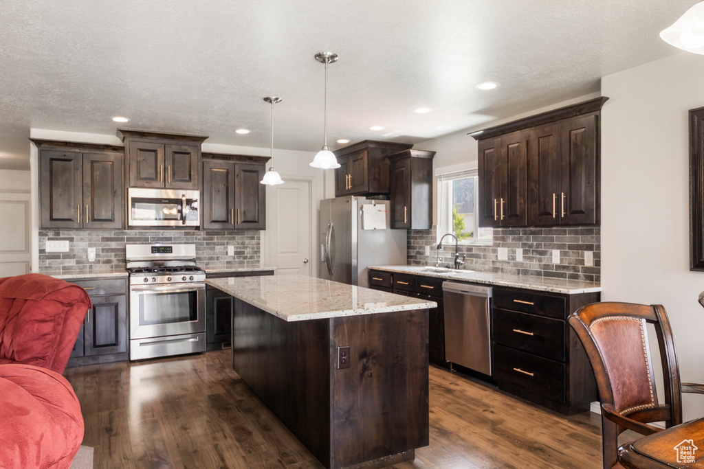 Kitchen with appliances with stainless steel finishes, dark wood-type flooring, dark brown cabinetry, a center island, and decorative backsplash
