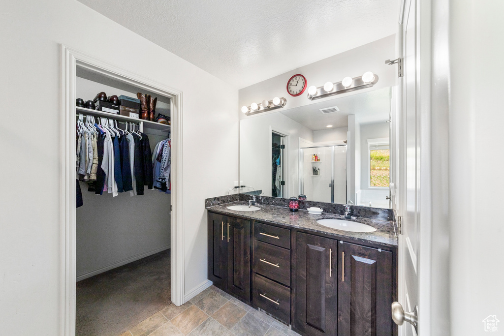 Full bathroom with a stall shower, a walk in closet, double vanity, baseboards, and stone finish floors
