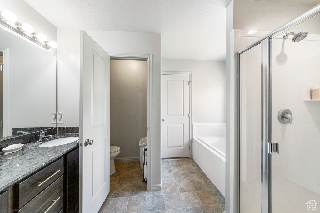 Bathroom featuring a stall shower, toilet, vanity, a garden tub, and baseboards