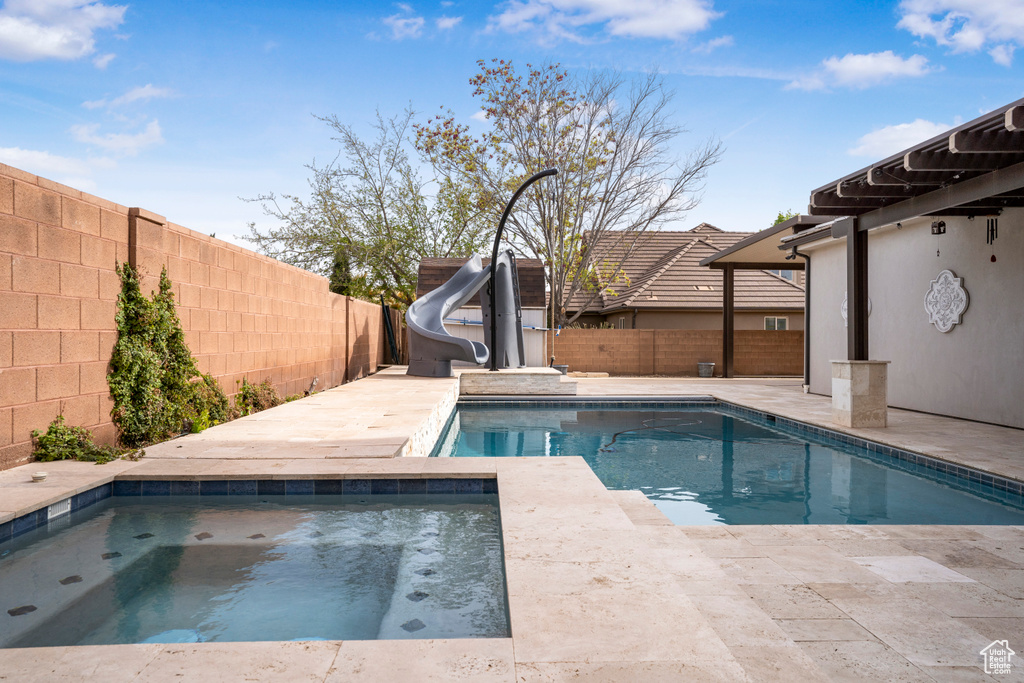 View of swimming pool featuring an in-ground hot tub, a water slide, and a fenced backyard