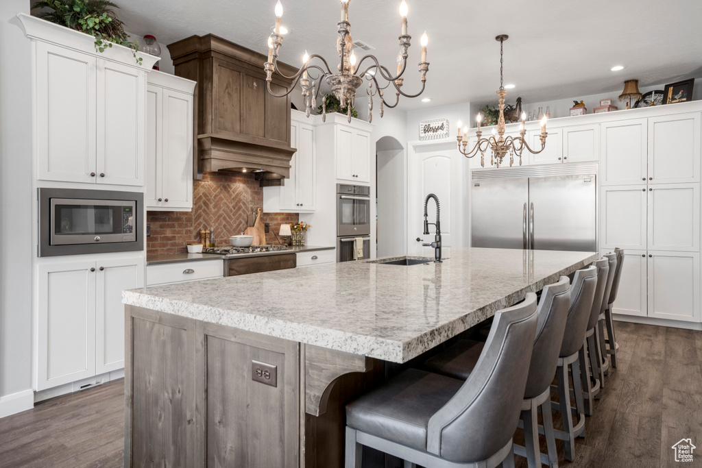 Kitchen with a chandelier, built in appliances, a sink, decorative backsplash, and a large island with sink